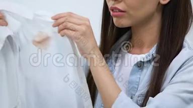不高兴的年轻女人看着衬衫上的咖啡污渍，无效的去斑剂